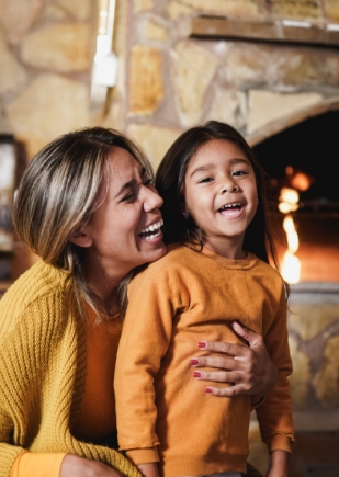 mother-hugging-little-daughter-near-fireplace-at-h-2021-12-09-15-34-29-utc